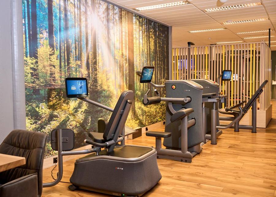 Mehrere EGYM-Trainingsgeräte mit Bildschirmen stehen im Trainingsbereich vor einer großflächigen Waldfototapete